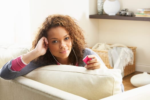 Woman Listening To MP3 Player On Headphones Relaxing Sitting On Rug At Home