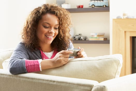 Woman Looking At Pictures On Digital Camera Relaxing Sitting On Sofa At Home
