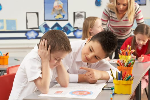 Group Of Primary Schoolchildren And Teacher Working At Desks In Classroom