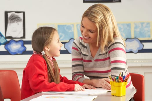 Female Primary School Pupil And Teacher Working At Desk In Classroom