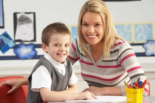 Male Primary School Pupil And Teacher Working At Desk In Classroom