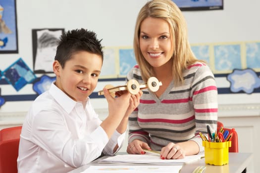 Male Primary School Pupil And Teacher Working At Desk In Classroom