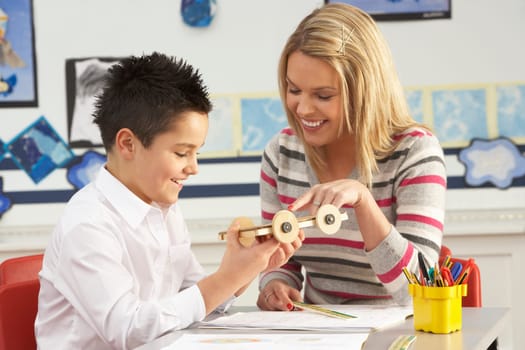 Male Primary School Pupil And Teacher Working At Desk In Classroom