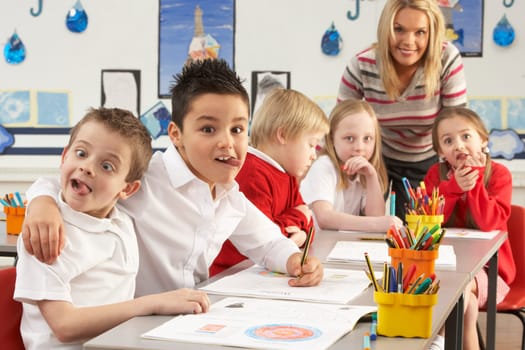 Group Of Primary Schoolchildren And Teacher Working At Desks In Classroom