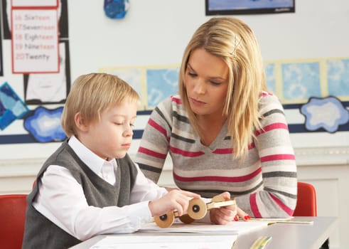 Male Primary School Pupil And Teacher Working At Desk In Classroom