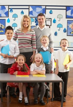 Portrait Of Group Of Primary Schoolchildren And Teachers Sitting At Desk In Classroom