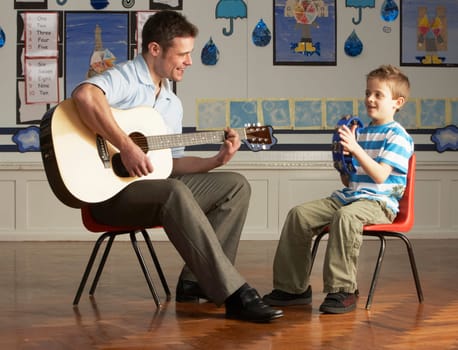 Male Teacher Playing Guitar With Pupil In Classroom