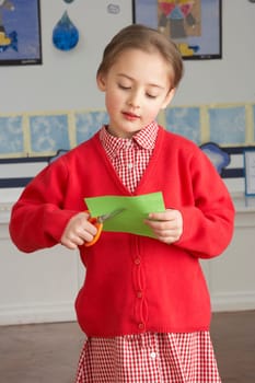 Female Primary School Pupil Cutting Out Paper Shapes In Craft Lesson