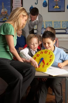 Female Teacher In Primary School Teaching Children To Tell Time In Classroom