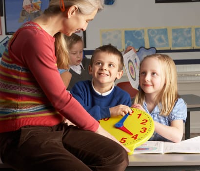 Female Teacher In Primary School Teaching Children To Tell Time In Classroom
