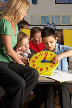 Female Teacher In Primary School Teaching Children To Tell Time In Classroom