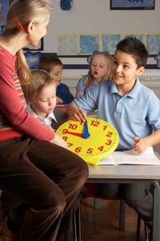 Female Teacher In Primary School Teaching Children To Tell Time In Classroom