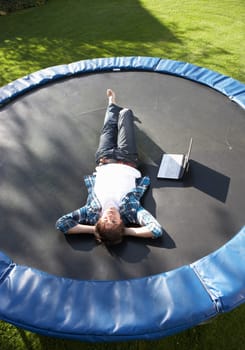 Young Man Relaxing On Trampoline With Laptop