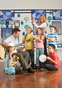 Teachers Playing Guitar With Pupils Having Music Lesson In Classroom