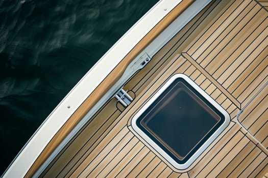 Wooden yacht deck with metal hatch and calm water view.