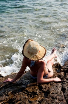 woman with hat sitting on rocks