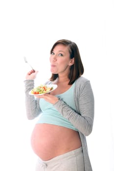 Pregnant woman eating healthy salad. She holds a plate and fork in her hand and enjoys her healthy food