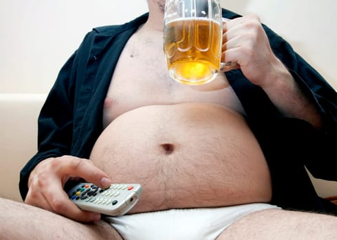 Overweight man sitting on the couch with a beer gl