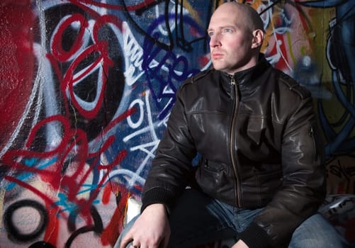 man with attitude in front of graffiti wall in urban area. mature middle aged man by street art in deprived town area