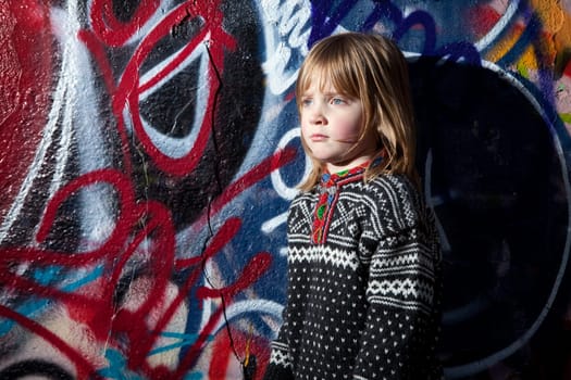 child in front of graffiti wall in urban area. Cool young boy by street art in deprived town area