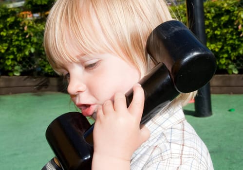 child on play toy telephone. blond kid outside playing game of pretend communication