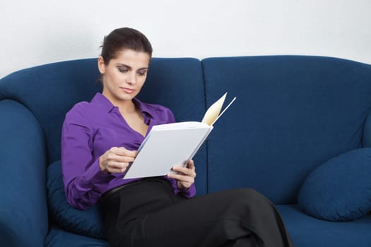 Young pretty businesswoman sitting on sofa in a waiting room and browing an album