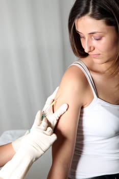 Young woman receives an injection at doctor. She receives the injection into the upper arm