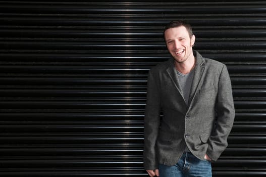 Portrait of a young man smiling dressed casually leaning against uniform dark background.