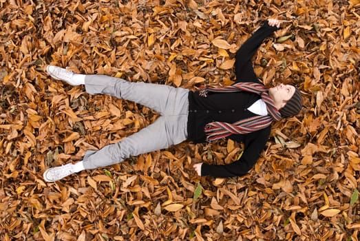 High angle full body shot of young man laying on the yellow leaves covered ground.