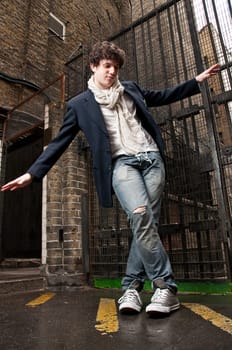 Low angle portrait of young man dancing in the street with metal gate in the background.