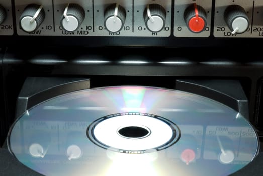 Detail shot of a CD in a player&#039 s drawer with crossover buttons on top. Front shot with dark background.