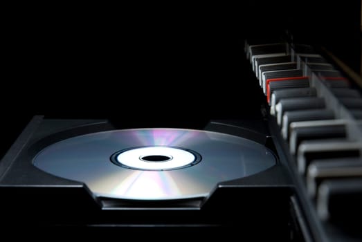 Detail shot of a CD in a player&#039 s drawer with crossover buttons on the top right, in perspective. Side shot with dark background.