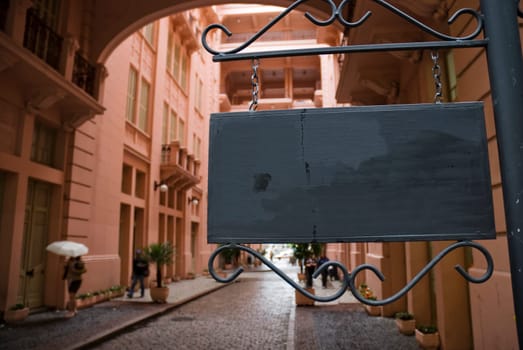 Dark wooden sign board with pink Victorian building in the background. Low angle shot.