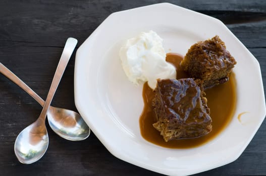 Sticky pudding and cream with silver spoon on wooden table