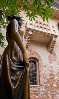 Low angle shot of statue of Juliet, with balcony in the background.