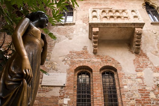 Low angle shot of statue of Juliet, with balcony in the background.