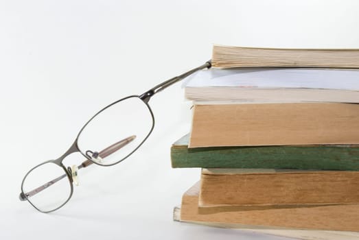 Detail shot of a pair of glasses with stack of books. White background.