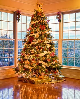 Christmas tree with presents and lights reflecting in windows around the tree in modern home