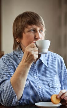 Elderly woman enjoying a cup of coffee and cookie at home