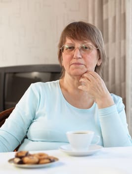 Elderly woman enjoying a cup of coffee with cookies at home