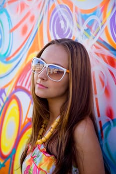 Young woman in glasses stand near graffiti wall