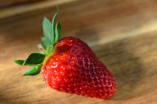 Juicy red strawberry showcases its vibrant color and textures on a rustic wooden table, inviting a scrumptious bite.