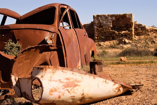 an old rusting car and ruins in the desert