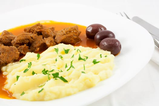 Goulash with mashed potato spiced with parsley and three brown olives.