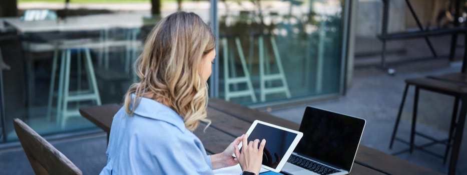 Portrait of businesswoman working on digital tablet, checking diagrams, sitting outdoors on fresh air near office building. Corporate woman prepare for work meeting.