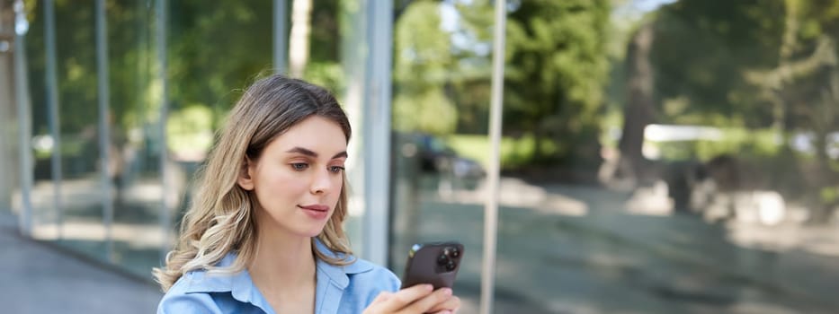 Vertical shot of successful businesswoman sitting outdoors in park, working on her project, using mobile phone. Corporate people concept.