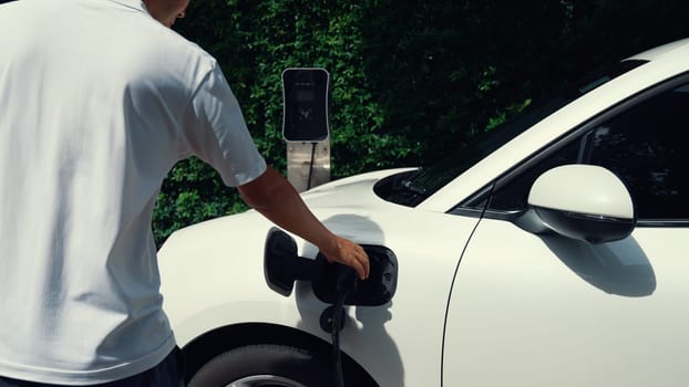 Progressive man install power cable plug to his electric vehicle, EV car from home charging station. Electric car driven by clean and renewable energy to preserve environment. Eco-friendly automobile.