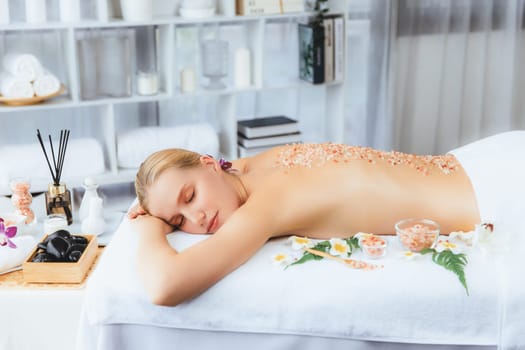 Woman customer having exfoliation treatment in luxury spa salon with warmth candle light ambient. Salt scrub beauty treatment in health spa body scrub. Quiescent