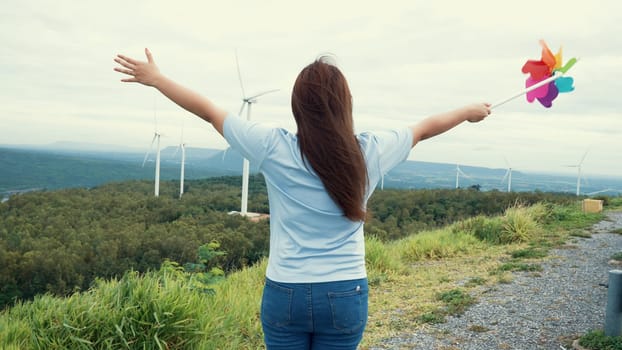 Concept of progressive happy woman enjoying her time at the wind turbine farm. Electric generator from wind by wind turbine generator on the country side with hill and mountain on the horizon.