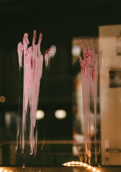 Portrait of bloody traces of adult hands on the glass of a window overlooking a blurred night landscape, side view close-up with selective focus.